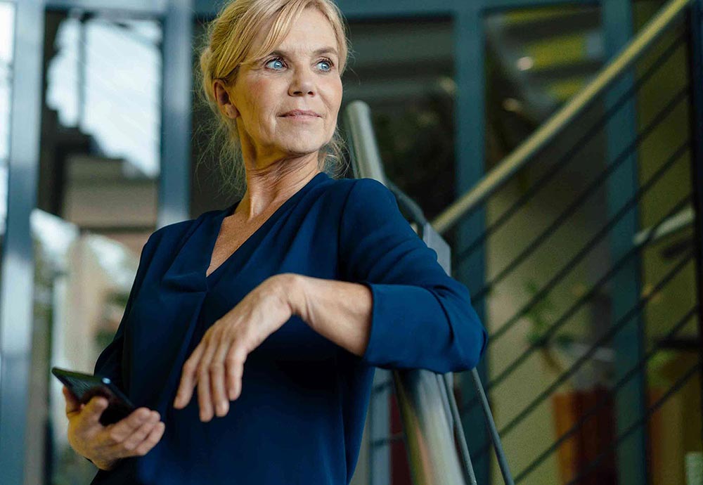 Frau lehnt sich an ein Treppengeländer, während sie entspannt und nachdenklich in die Ferne schaut.