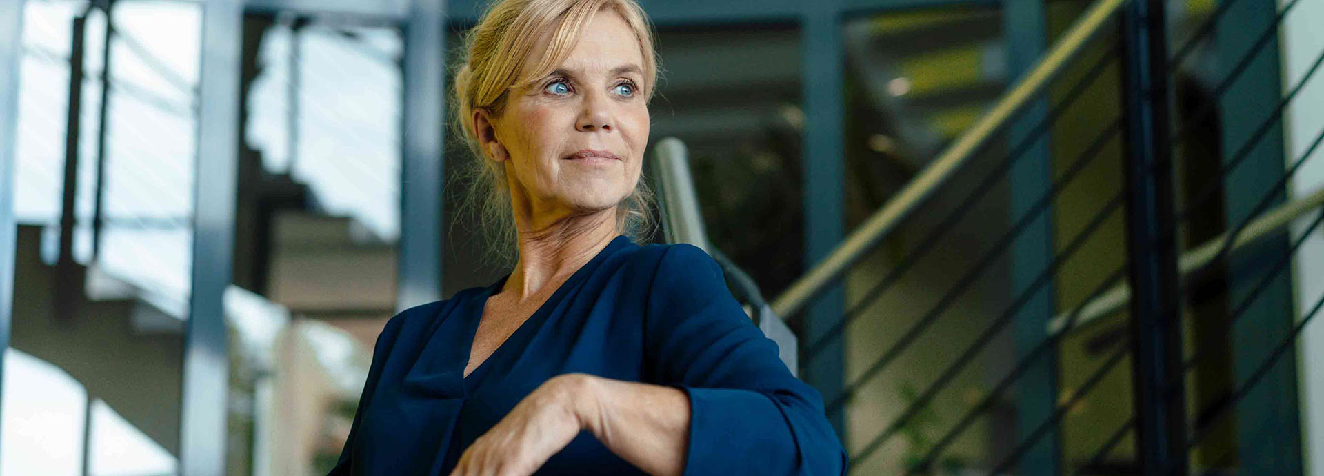 Frau lehnt sich an ein Treppengeländer, während sie entspannt und nachdenklich in die Ferne schaut.