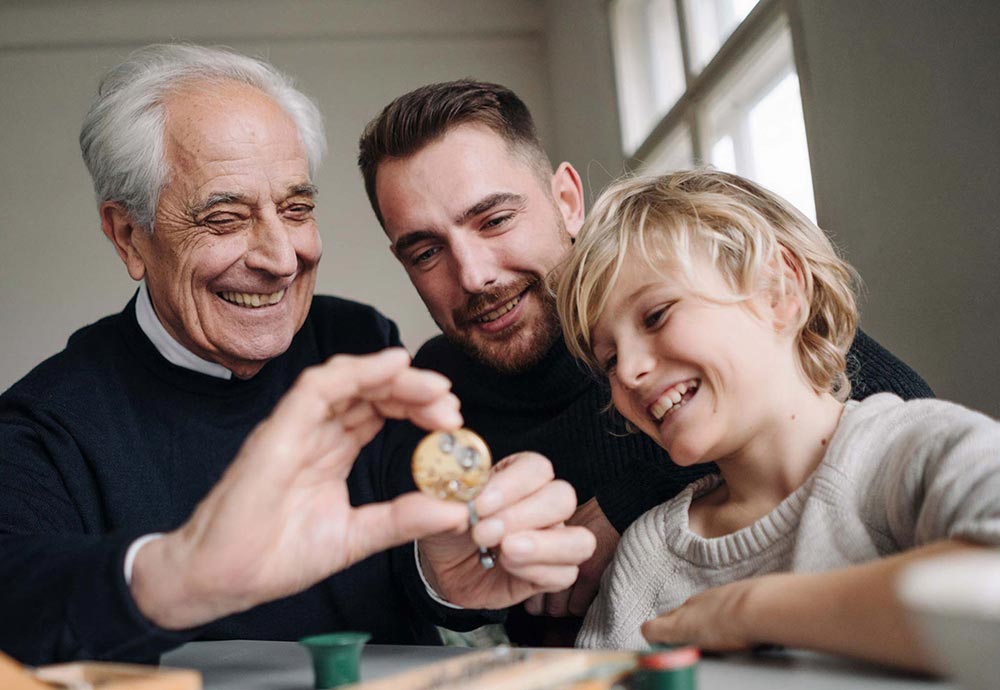 Drei Generationen, Großvater, Vater und Kind, lachen gemeinsam und schauen auf eine Münze, die der Großvater in der Hand hält.