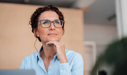 Eine Frau mit Brille schaut in die Ferne und stützt ihr Kinn mit der Hand.