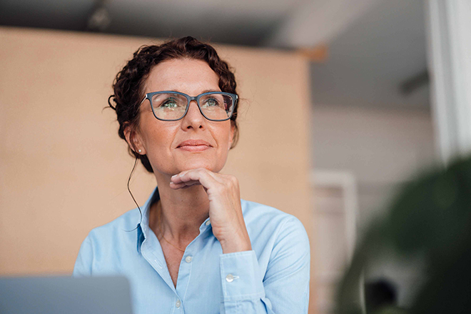 Eine Frau mit Brille schaut in die Ferne und stützt ihr Kinn mit der Hand.